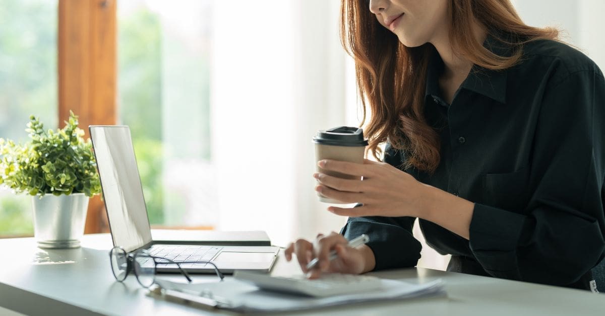 woman holding coffee and typing on calculator